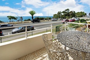 A balcony with a view of a road and ocean, a metal table, and a patterned railing. - Headlands 16 Ocean View Holiday (Alexandra Headland)