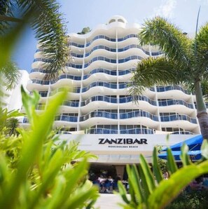 Un hôtel à plusieurs étages doté de balcons, offrant une vue sur la plage, et sur lequel on peut lire l’inscription « ZANZIBAR MOOLOLABA BEACH ».