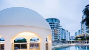 Ein modernes Hotel mit Pool, einer kuppelförmigen Struktur und Hochhäusern im Hintergrund.