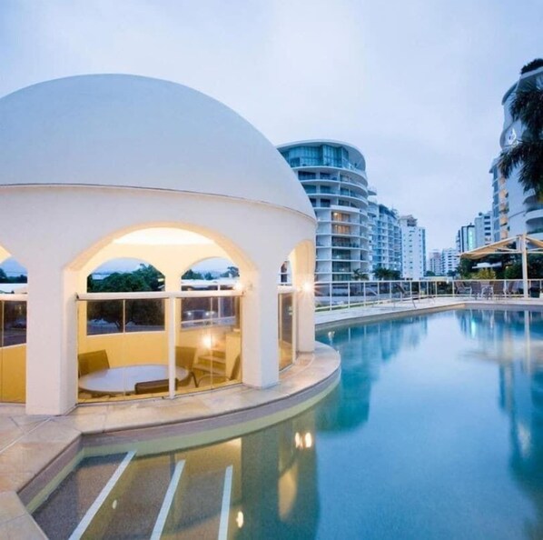 Un hôtel moderne doté d’une piscine, d’une structure en forme de dôme et de bâtiments de grande hauteur en arrière-plan.