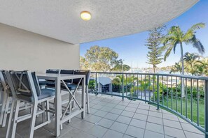 A balcony with a table and chairs, a railing, and a view of palm trees and buildings. - Riverdance 06 Riverfront Apt (Mooloolaba)