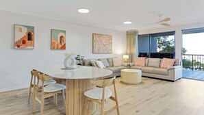 Uma sala de estar moderna com uma mesa de jantar redonda, cadeiras de madeira, um sofá, uma mesa de centro e obras de arte nas paredes.