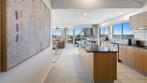 A modern kitchen with a large island, a dining area with a view, and a staircase leading to an upper level. - Luxurious Penthouse Near Beach with Unmatched Views (Mooloolaba)