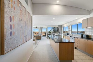Eine moderne Küche mit einer großen Kochinsel, ein Essbereich mit Blick und eine Treppe, die zu einer oberen Ebene führt.