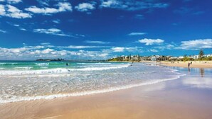 A beach with clear skies, waves, and distant buildings. - Luxurious Penthouse Near Beach with Unmatched Views (Mooloolaba)