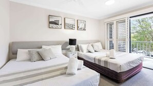 Une chambre d’hôtel avec deux lits, un ventilateur de plafond, une table de chevet et une fenêtre avec des stores.