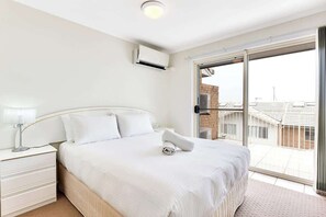 A bedroom with a bed, a nightstand, a lamp, and a view of the outside.