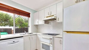 A compact kitchen with white cabinets, a built-in oven, a sink, and a window with a view of greenery outside.