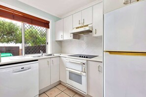A compact kitchen with white cabinets, a built-in oven, a sink, and a window with a view of greenery outside.