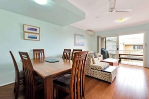 A dining area with a wooden table and chairs, a sofa, and a balcony with a view.