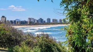 A coastal cityscape with high-rise buildings, a beach, and dense greenery.