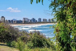 A coastal cityscape with high-rise buildings, a beach, and dense greenery.