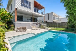 A modern two-story house with a swimming pool, outdoor seating, and a fenced backyard.