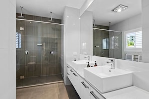 Ein modernes Badezimmer mit Duschkabine aus Glas, zwei Waschbecken und einem großen Spiegel.
