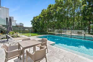 A swimming pool with a patio area, surrounded by trees and a fence.