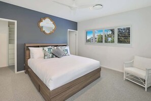 Ein Schlafzimmer mit einem Bett, einem weißen Stuhl, einem Kleiderschrank, einem Deckenventilator und einem Fenster mit Jalousien.