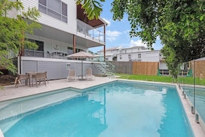 Ein modernes, zweistöckiges Haus mit Pool, Sitzgelegenheiten im Freien und einem Holzzaun.