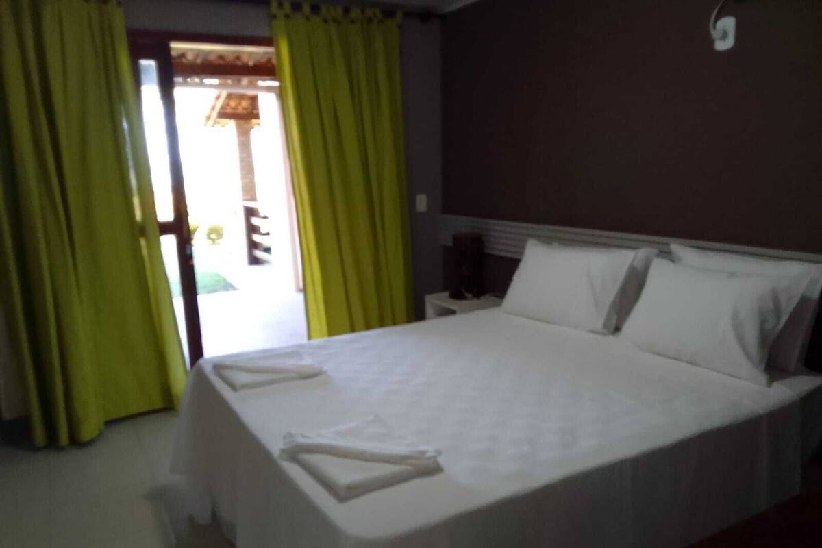 A neatly made bed in a hotel room with a headboard, a nightstand, and a window with curtains.