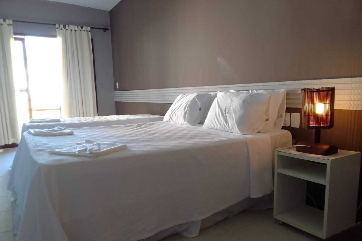 A hotel room with two beds, white linens, a bedside lamp, and a nightstand.
