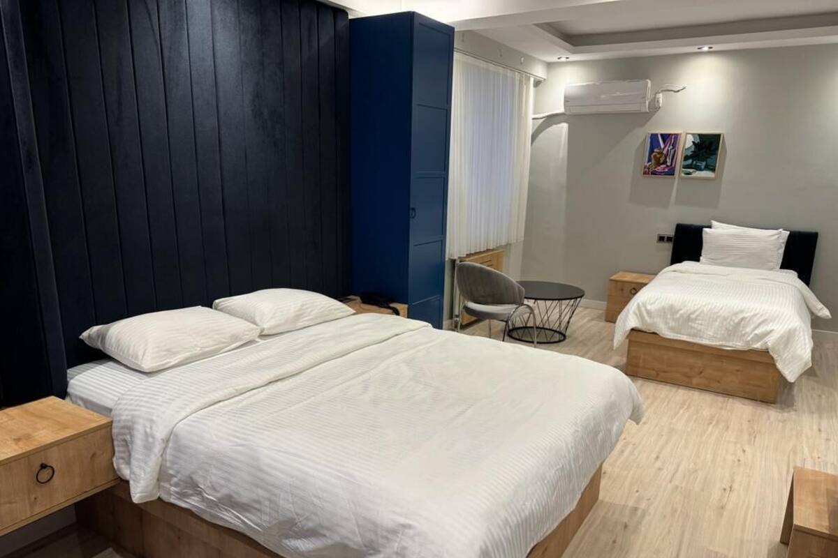 A modern hotel room with a large bed, a smaller bed, a desk, and a chair.