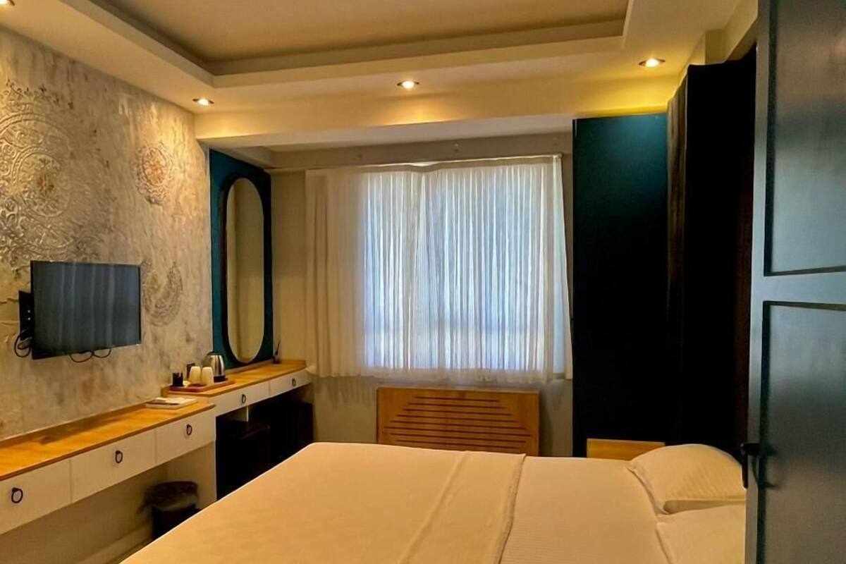A modern bedroom with a large bed, a vanity with a mirror, and a flat-screen TV mounted on the wall.