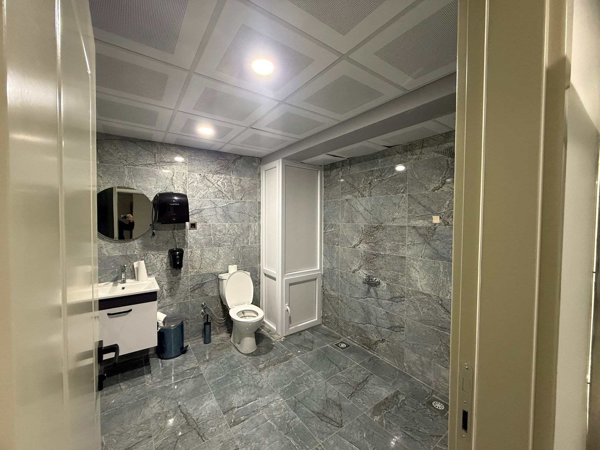 Ein modernes Badezimmer mit Marmorboden, Toilette, Waschbecken inklusive Spiegel und einer Duschkabine.