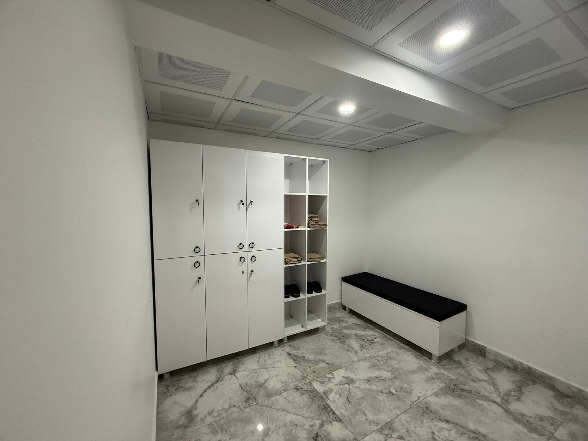 Une pièce avec une armoire blanche, des étagères et un banc.