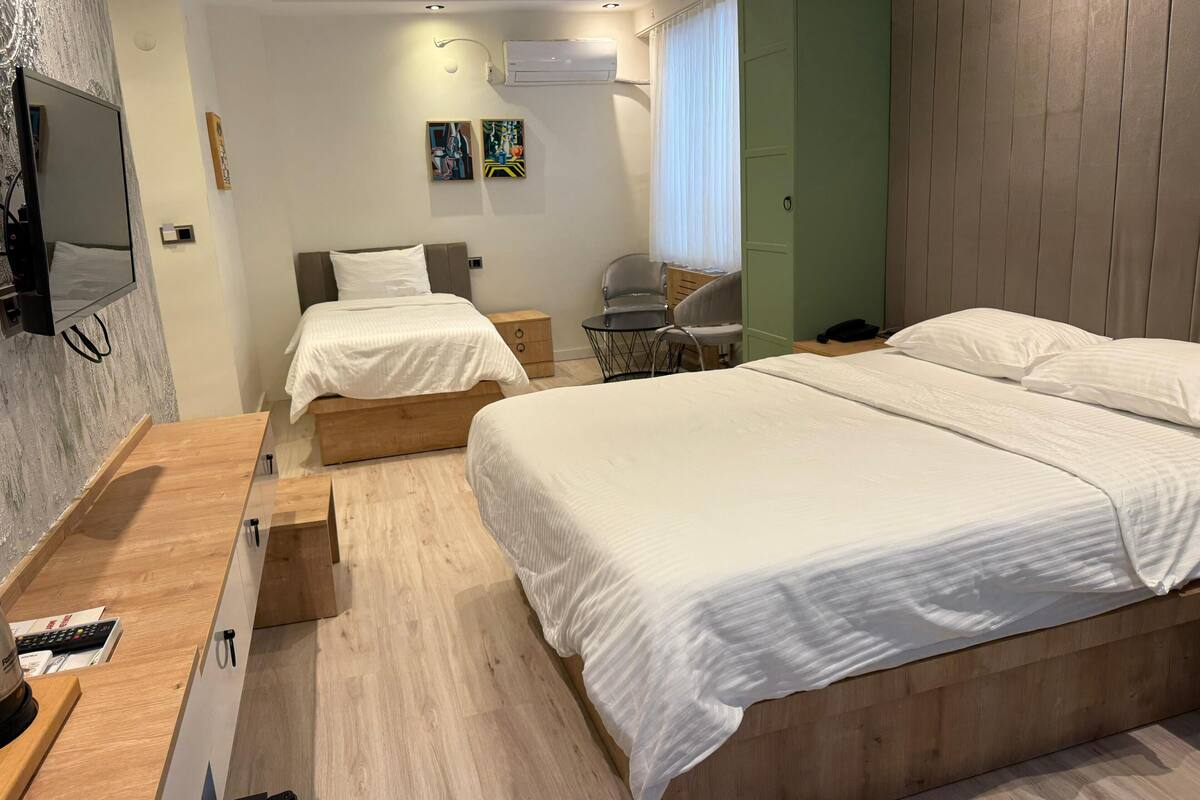 A modern hotel room with a large bed, a desk with a chair, a TV mounted on the wall, and artwork on the wall.