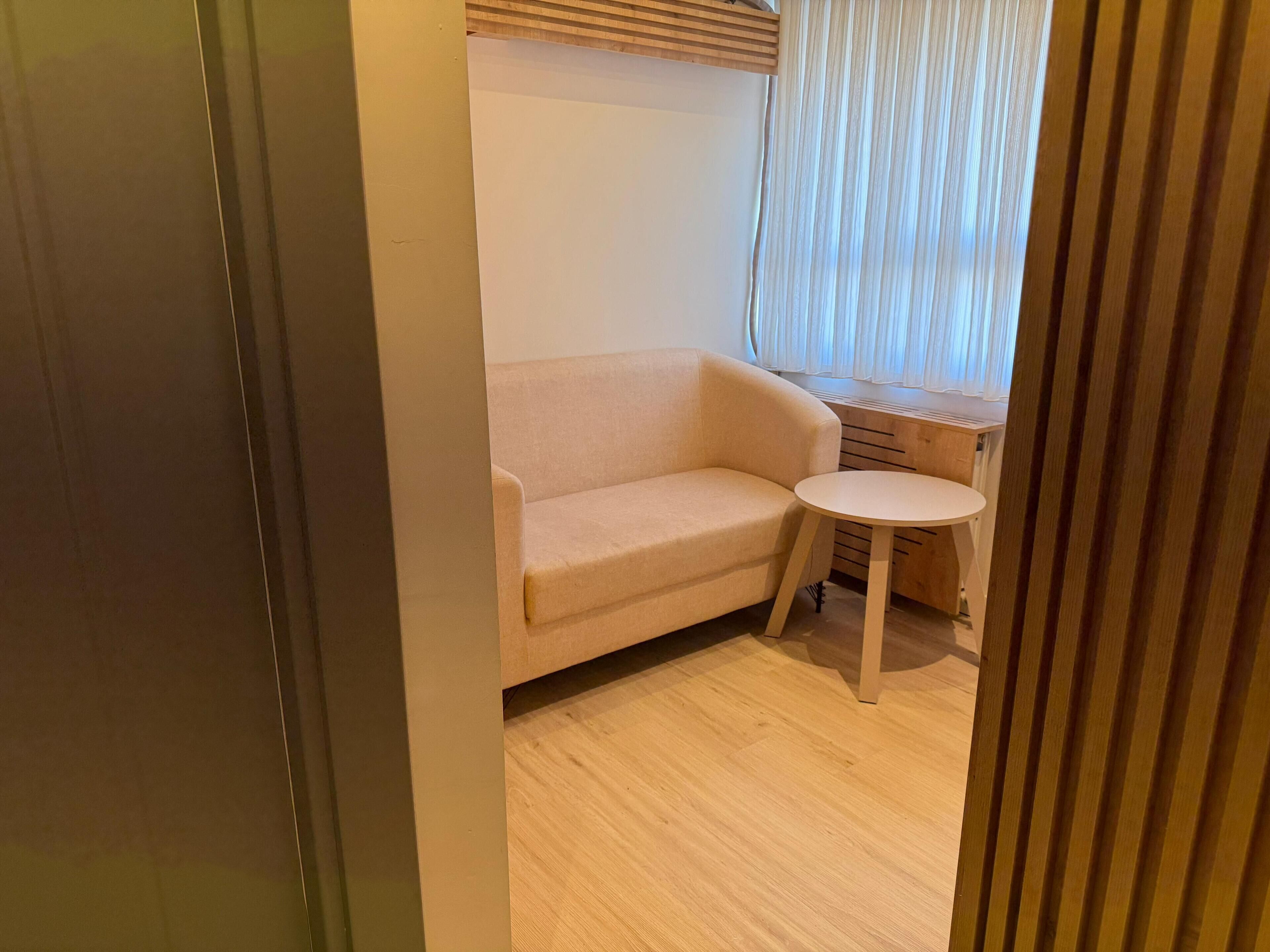A room with a beige sofa, a small round table, and a wooden desk.