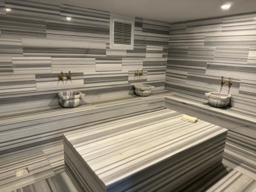 Un baño moderno con salpicadero de mármol, un lavabo central y dos lavamanos.