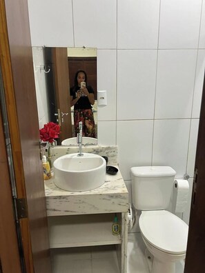 Een badkamer met een wit wastafel, toilet en een spiegel die iemand weerspiegelt.