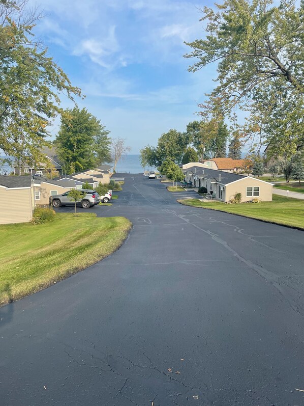 Una calle residencial con casas, coches aparcados y una vista despejada del agua al fondo.