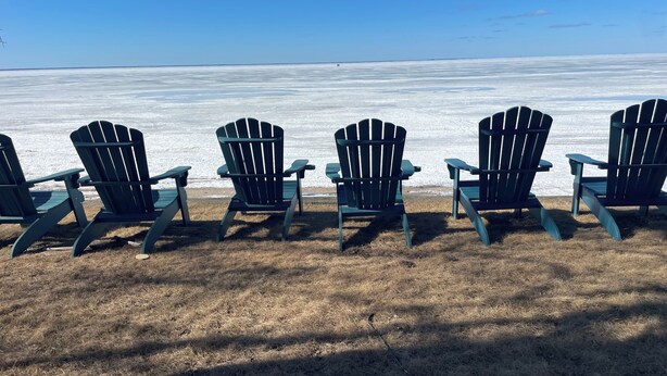 Vier Adirondack stoelen op een gazon met uitzicht op een bevroren waterlichaam onder een heldere lucht.