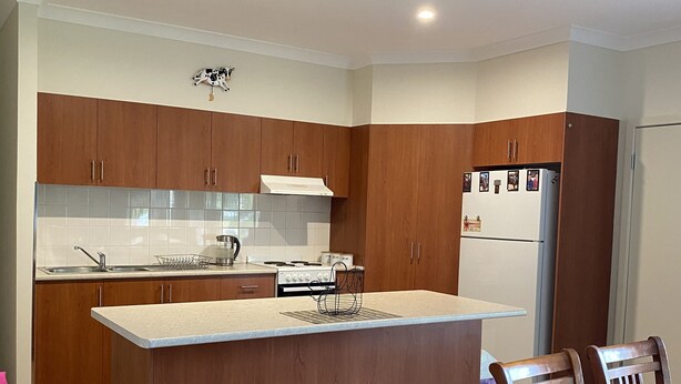 Una cocina moderna con armarios de madera, una isla central y un comedor con sillas de madera.