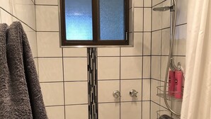Pequeño espacio de ducha con azulejos, una ventana, un perchero y un cabezal de ducha.