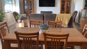 Un comedor con una mesa y sillas de madera, un televisor montado en la pared y un armario con puertas de cristal.