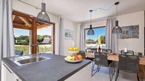 Een moderne keuken met een groot kookeiland, een eethoek met een tafel en stoelen, en uitzicht op de omgeving.
