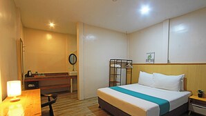 Habitación de hotel con cama, mesita de noche, escritorio, silla y una pequeña mesa con lámpara.