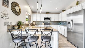 Una cocina moderna con armarios blancos, un refrigerador de acero inoxidable, una isla grande con taburetes y luces colgantes.