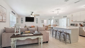 A modern living room with a sofa, a coffee table, and a kitchen area with a bar and stools. - Bikes, Yard & Fire Pit at Upscale Lecanto Home! (Lecanto)