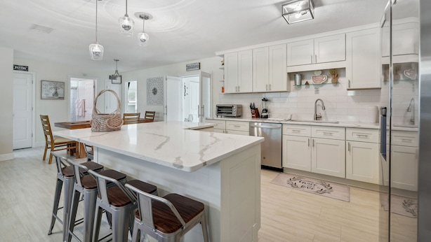 A modern kitchen with white cabinets, a central island with stools, stainless steel appliances, and pendant lighting. - Bikes, Yard & Fire Pit at Upscale Lecanto Home! (Lecanto)