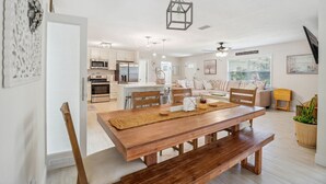 A modern kitchen with white cabinets, a central island, and a dining area with a wooden table and benches. - Bikes, Yard & Fire Pit at Upscale Lecanto Home! (Lecanto)