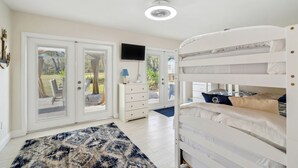 A bedroom with a bunk bed, a television on the wall, and a view of the outdoors through the door. - Bikes, Yard & Fire Pit at Upscale Lecanto Home! (Lecanto)