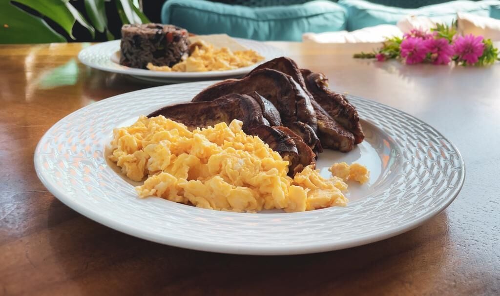 Ein Teller mit Rührei und Steak auf einer Holztischplatte.