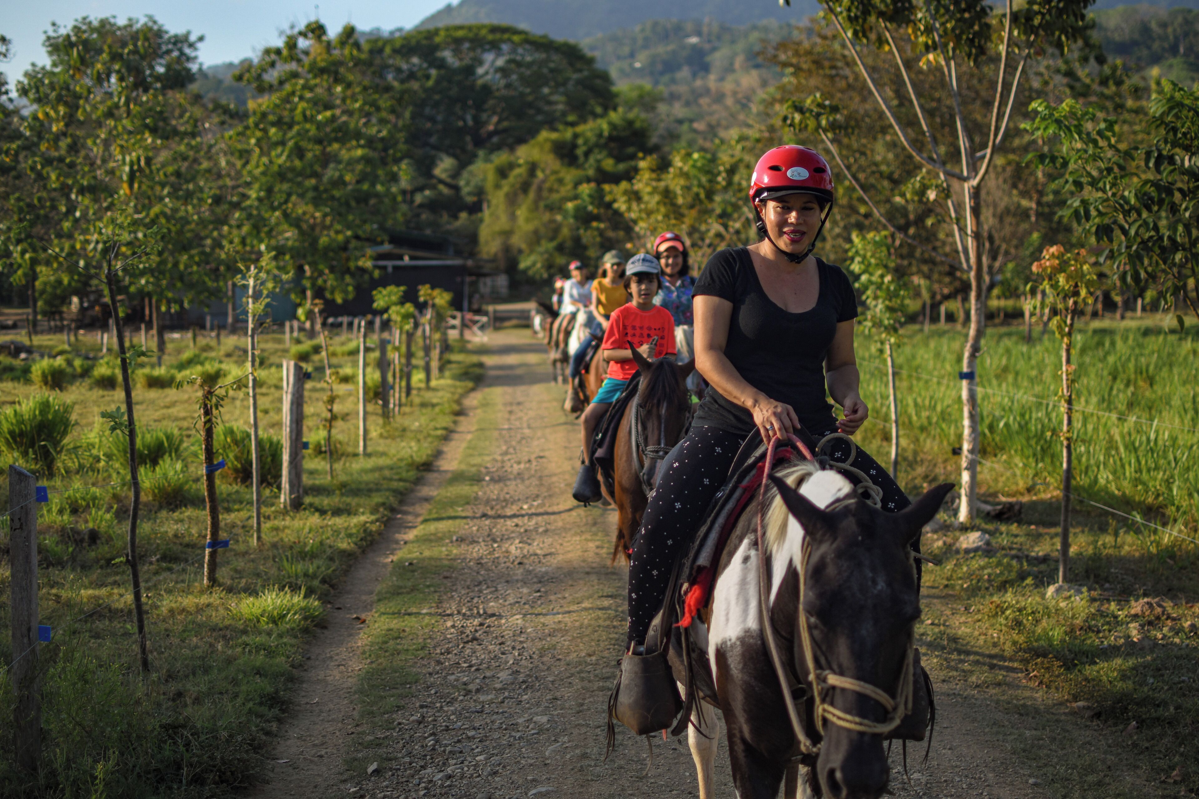 A group of people riding horses on a dirt path surrounded by greenery and trees.