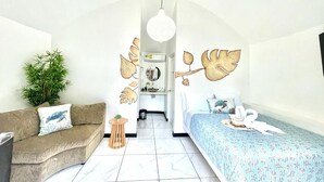 A room with a sofa, a bed, a small table, and a potted plant.