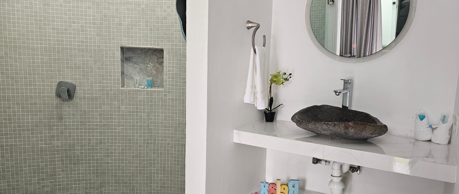 A bathroom with a tiled wall, a small window, a towel rack, a round mirror, a sink with a stone basin, and a potted plant.