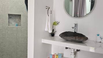 A bathroom with a tiled wall, a small window, a towel rack, a round mirror, a sink with a stone basin, and a potted plant.
