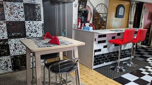 Zona de bar con suelo a cuadros, taburetes rojos y una barra con varios objetos.