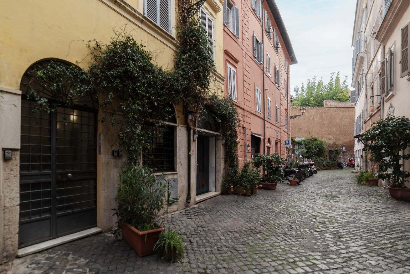 A cobblestone street with buildings on either side, featuring arched windows and doorways, and potted plants.